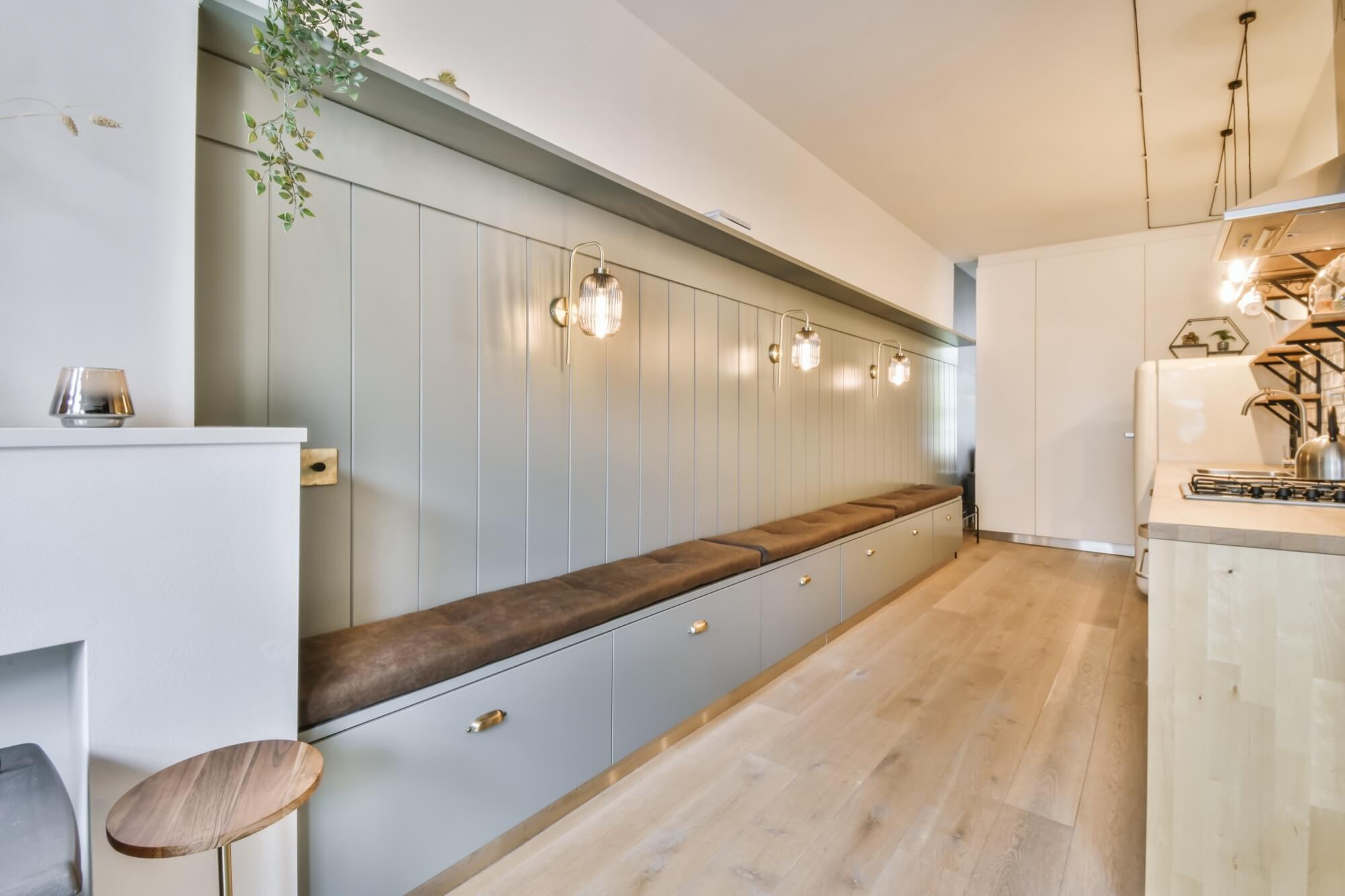 En lång, platsbyggd bänk i salviagrönt med förvaring och bruna dynor, ett smart snickerijobb för en hall eller ett kök.