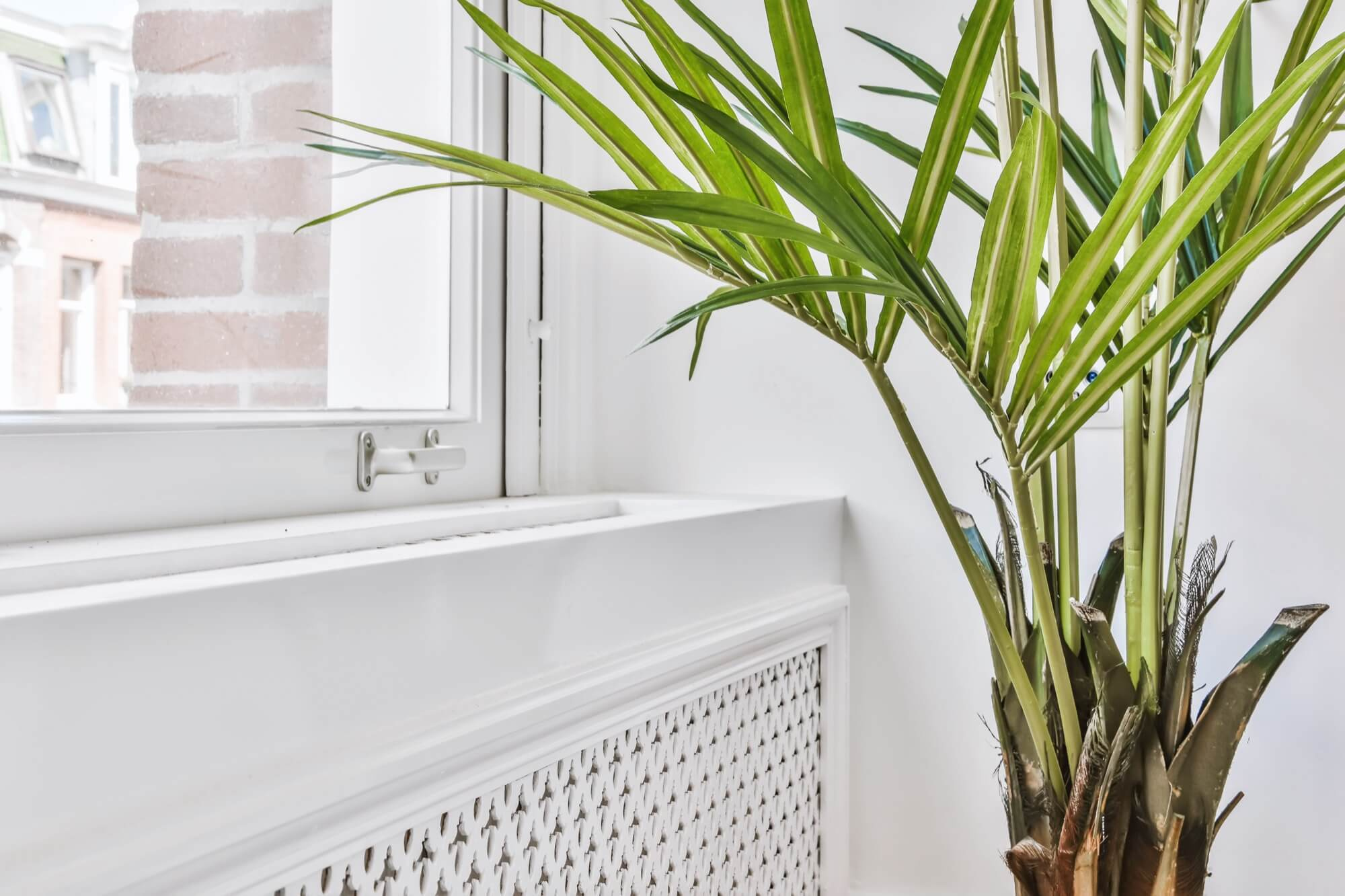 Ett specialbyggt vitt elementskydd installerat av en snickare under ett fönster, med en grön växt som dekoration.