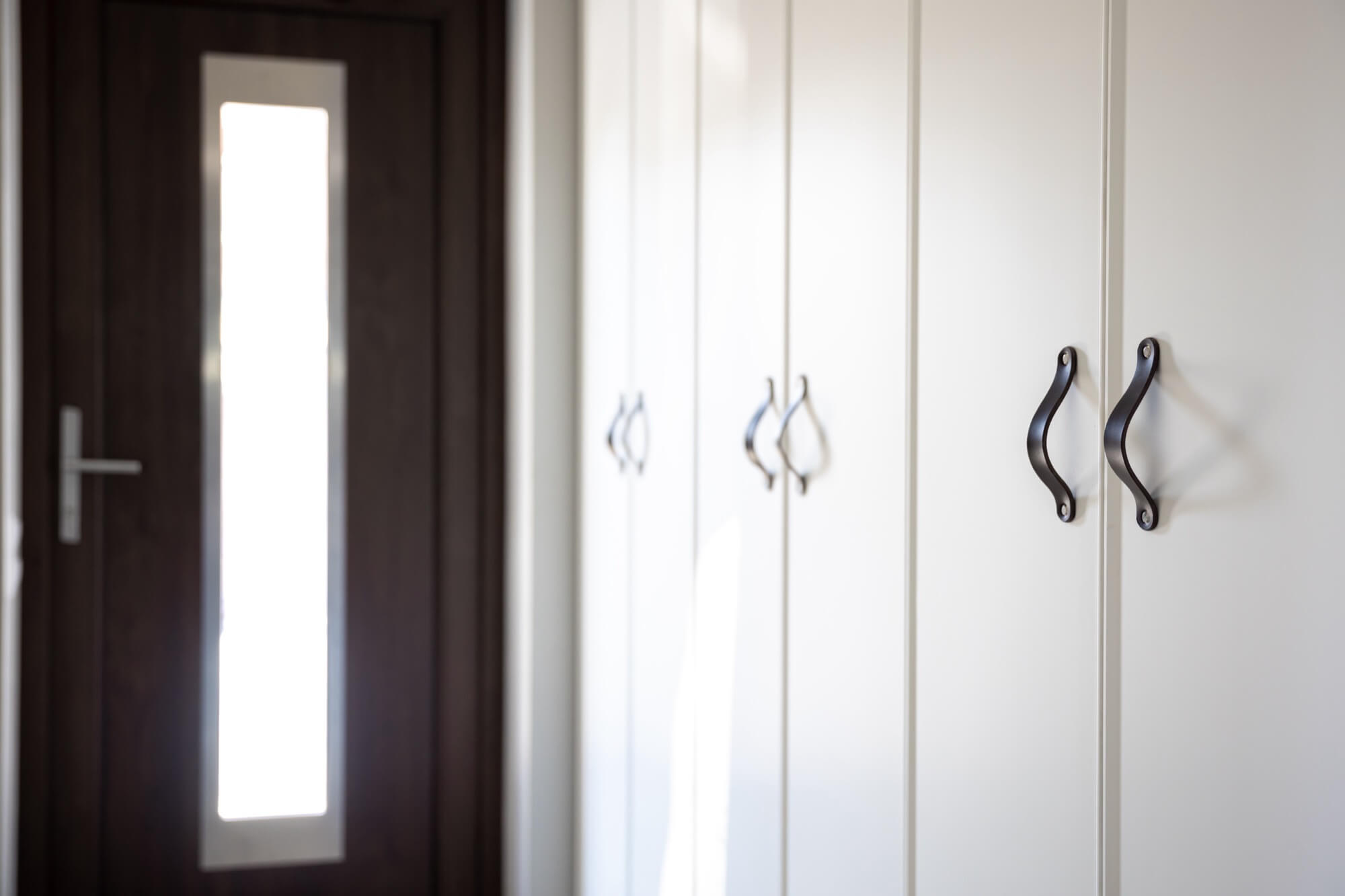 En rad med släta, vita garderober med svarta handtag, installerade av en snickare för att skapa maximal förvaring.